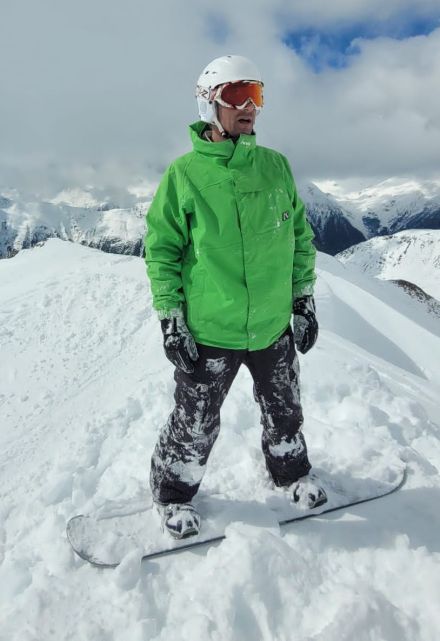 A Snowboarder in a green jacket standing on top of a white snow covered mountain